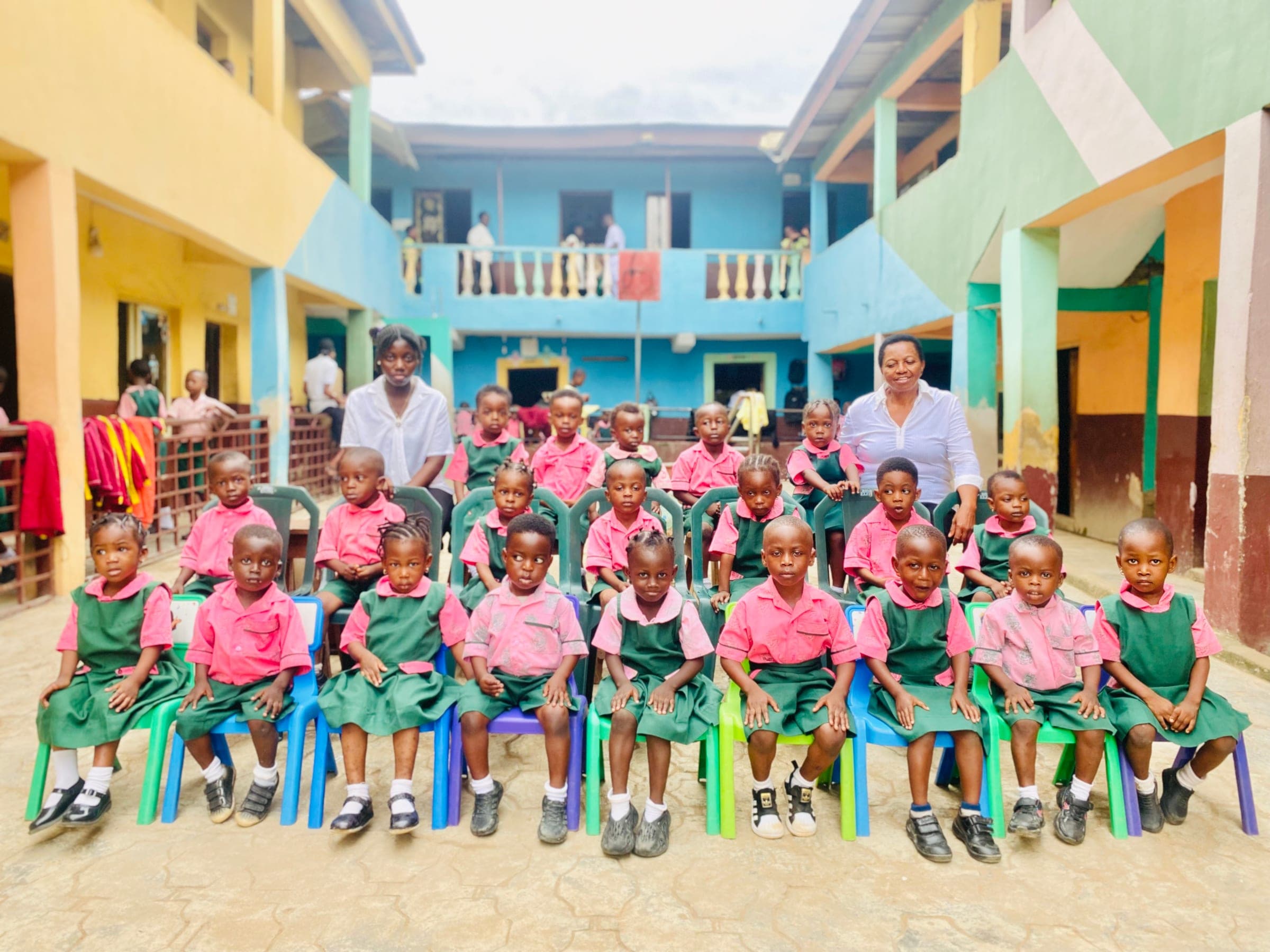 Youngest pupils of the school seated on coloured chairs with their two teachers