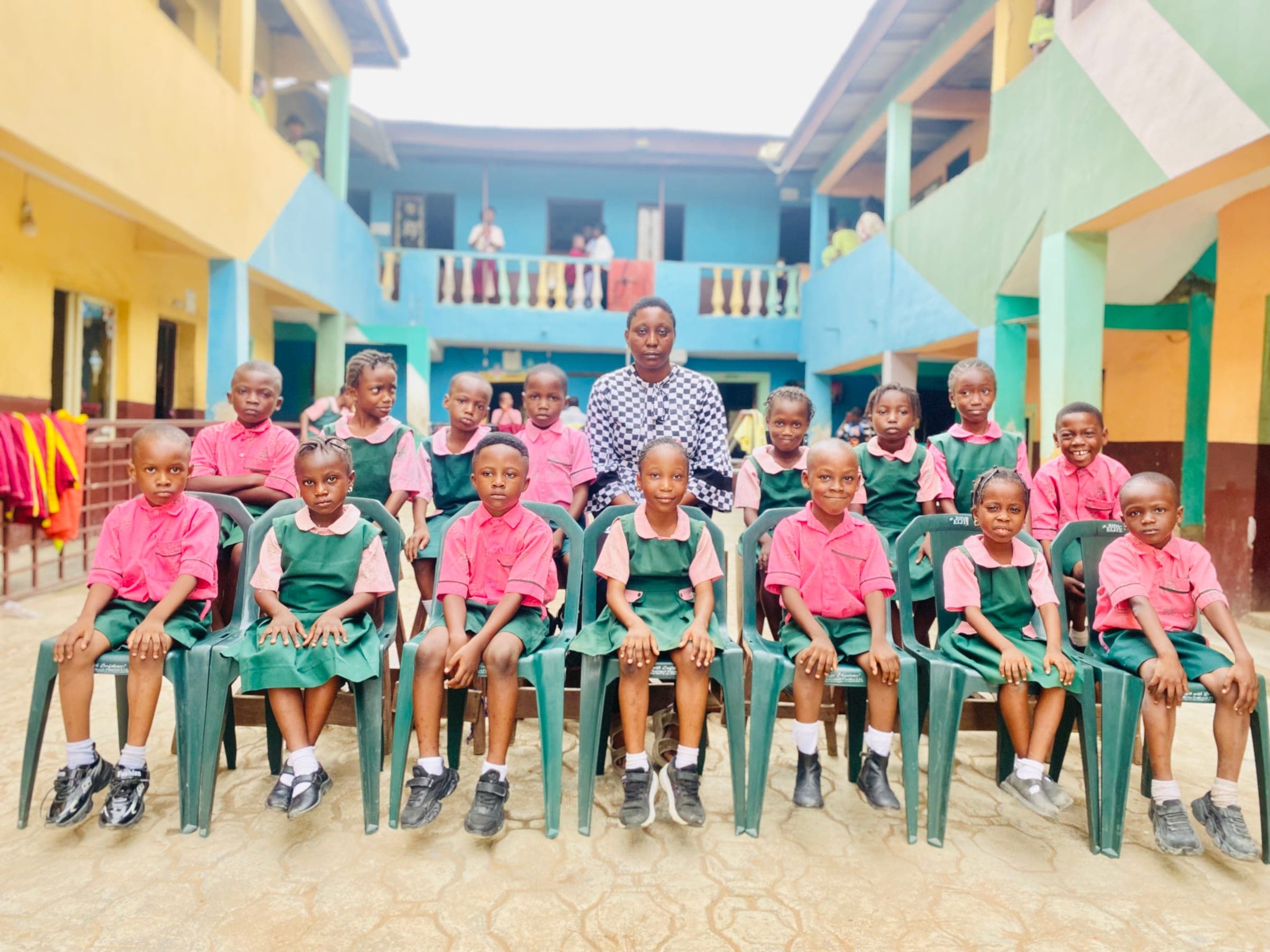 Primary pupils in green and pink uniform seated with their class teacher